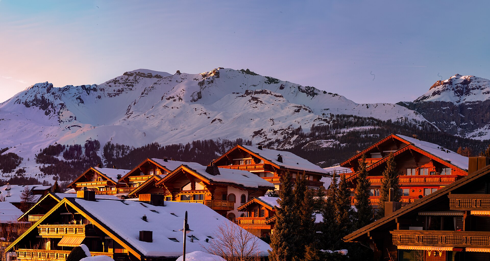Chalets enneigés de Crans-Montana à l'heure dorée, sommets alpins en arrière-plan